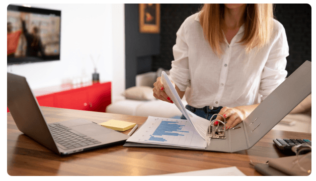 Woman reviewing a financial chart in a binder next to an open laptop
