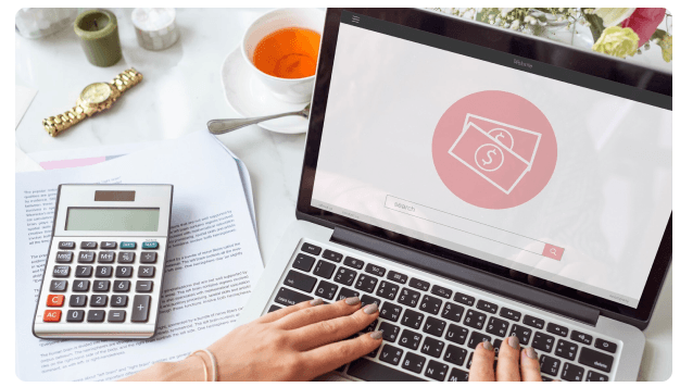Laptop displaying a money icon beside a calculator and a cup of tea