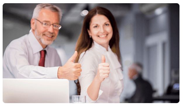 Two colleagues smiling and giving a thumbs up beside a laptop