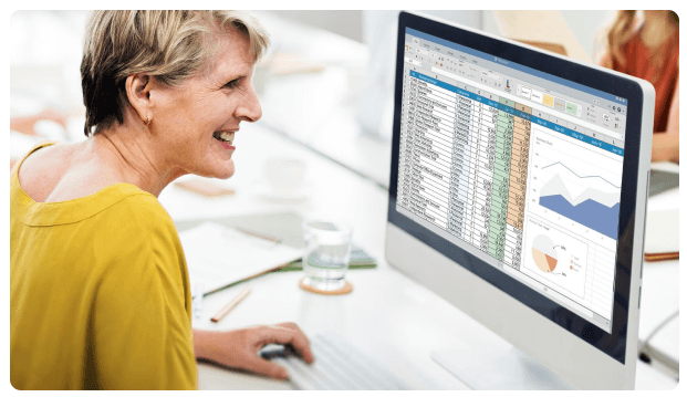 Woman reviewing spreadsheet charts and data on a desktop monitor