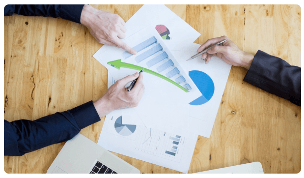 Two people reviewing financial charts and pie graphs on a desk
