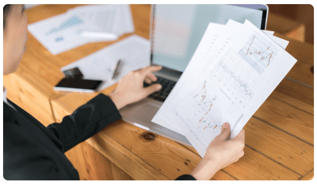 Businessperson reviewing printed financial charts beside an open laptop