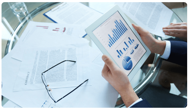 Hands holding a tablet displaying financial charts at a meeting table