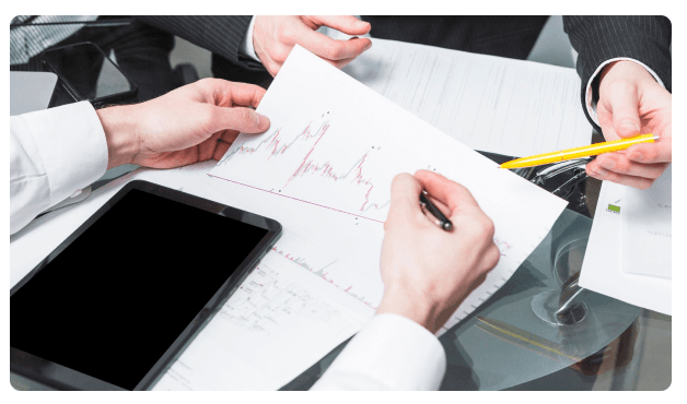 Two colleagues reviewing a hand-drawn financial chart with a tablet and pen on a glass table