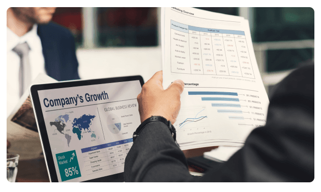 Businessman holding a tablet showing 'Company's Growth' beside printed reports and charts