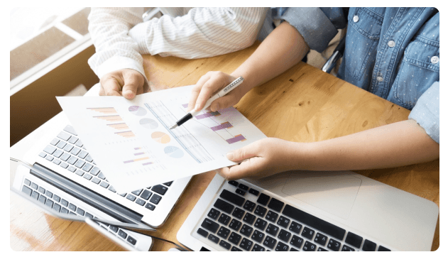 Hands reviewing colorful financial charts beside open laptops
