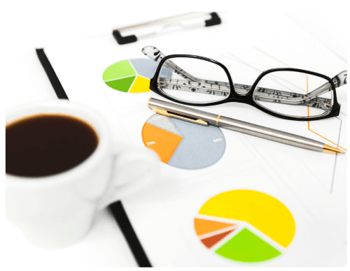 Desk with glasses, pens, coffee and financial pie charts