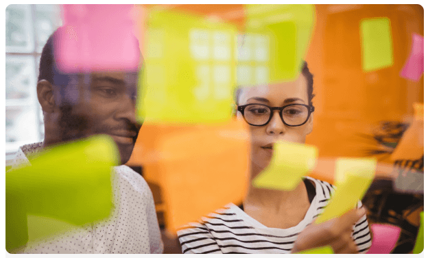 Colleagues reviewing sticky notes on a glass board