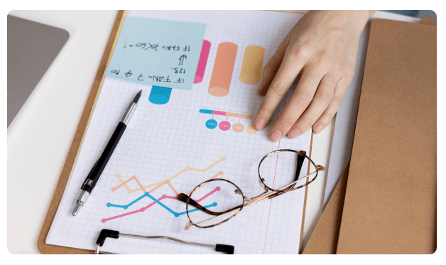 Hand pointing at a colorful bar chart with sticky notes and glasses on a desk
