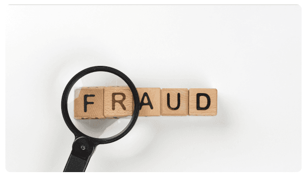 Magnifying glass over wooden blocks spelling the word 'Fraud'