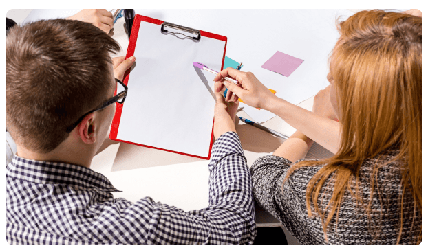 Two colleagues reviewing a document on a red clipboard