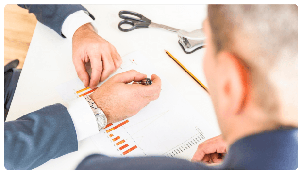 Hands reviewing a bar chart printout with a pen and scissors on a desk