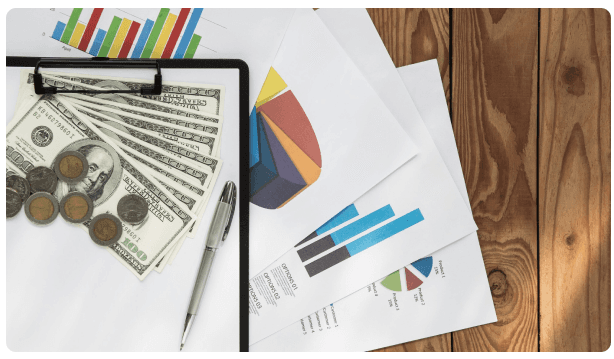 Clipboard with financial charts beside stacks of cash and coins