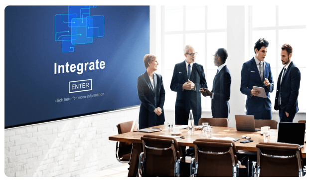 Team meeting in a boardroom in front of a screen reading Integrate