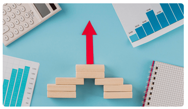Red arrow rising above stacked wooden blocks beside bar charts and a calculator