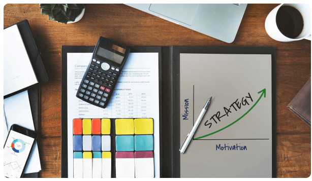 Desk with a calculator, planner, and a sticky note reading Strategy