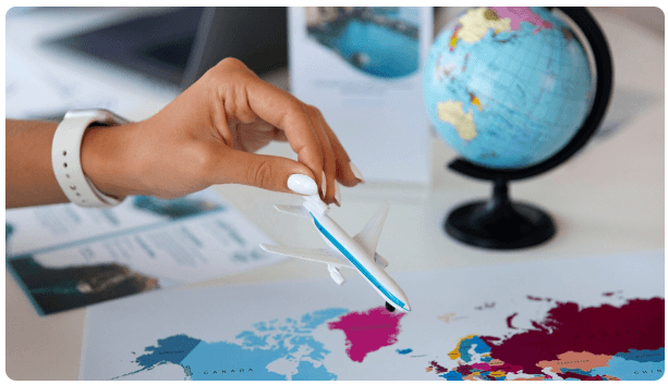 Hand placing a toy airplane on a world map beside a globe