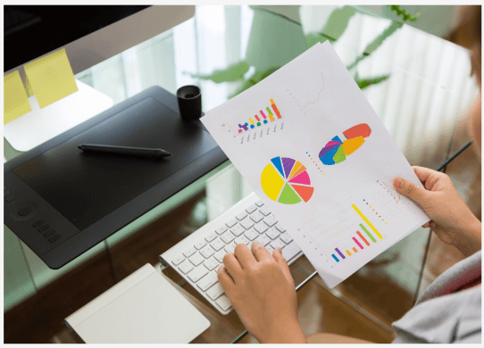 Hands reviewing colorful pie charts and bar graphs printed on paper