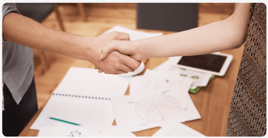 Two people shaking hands over documents on a desk
