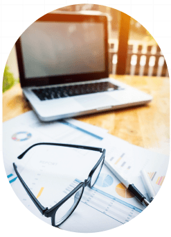 Glasses resting on financial reports beside a laptop