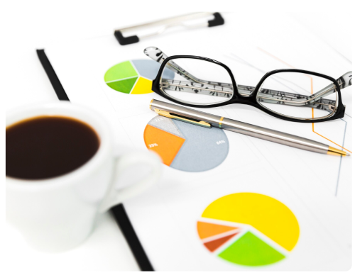 Desk with glasses, pens, coffee and financial pie charts